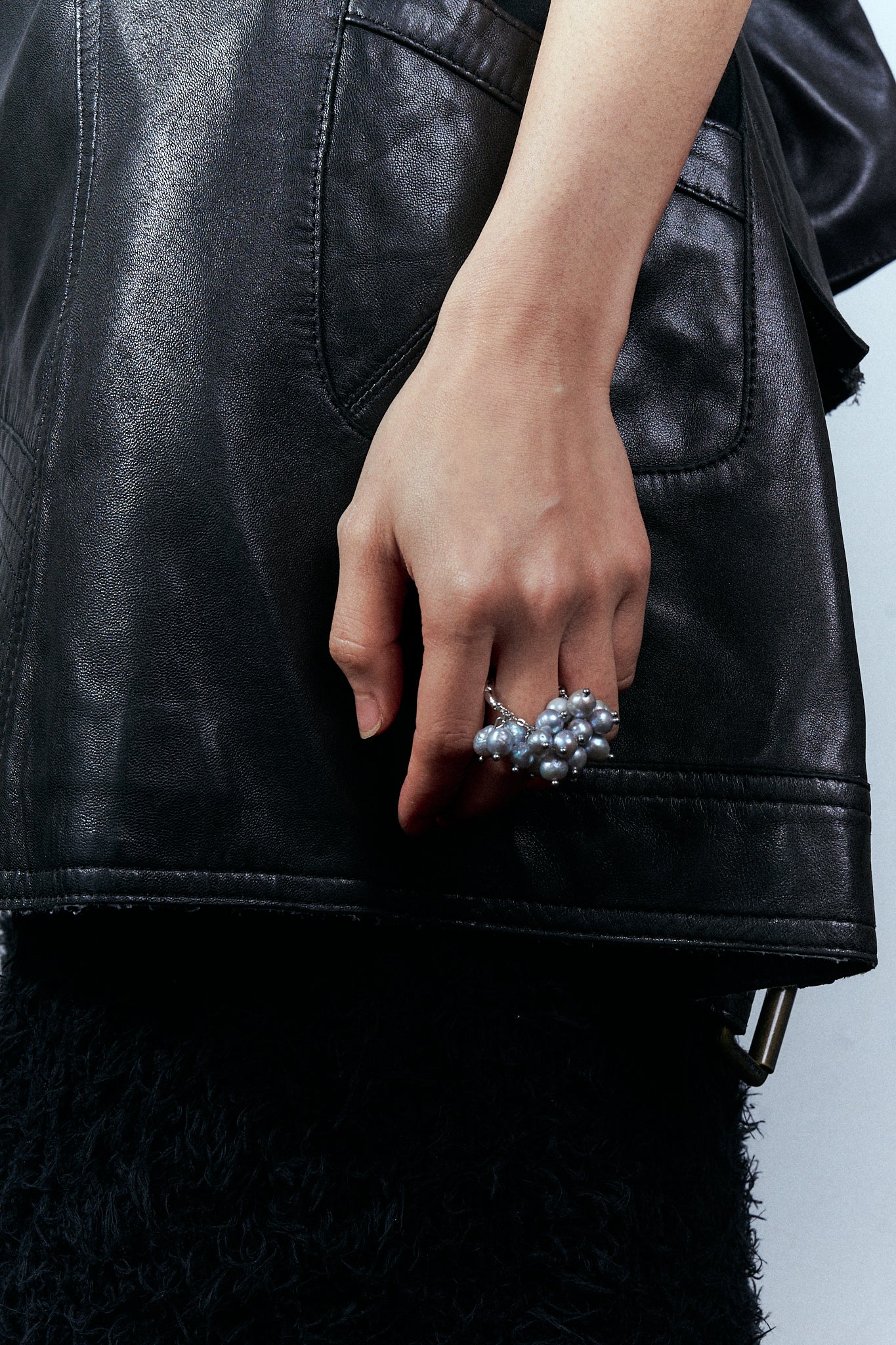 Person wearing a black leather jacket with a hand wearing a pearl ring.